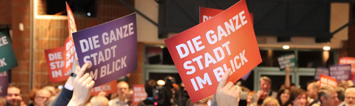 Foto: SPD-Anhänger heben Schilder mit Aufschrift "Die ganze Stadt im Blick" in die Luft