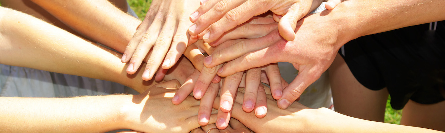 Foto: Menschen halten Hände übereinander als Symbol für Zusammenhalt